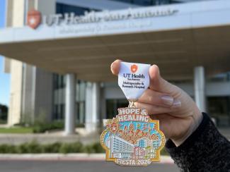 2026 hospital Fiesta medal being held in front of the main hospital entrance